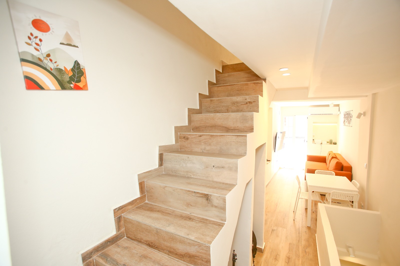 Wood-look stairs rising into a white living and dining room with an orange sofa at the far end.