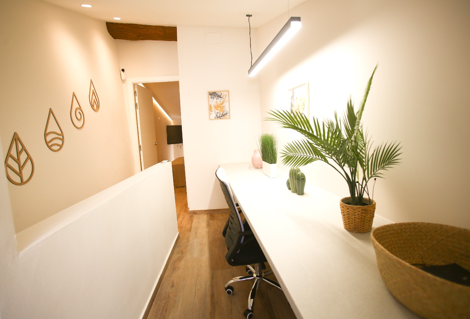 A built-in desk in a narrow hall, a linear lamp above it, an old wooden beam kept over the doorway.