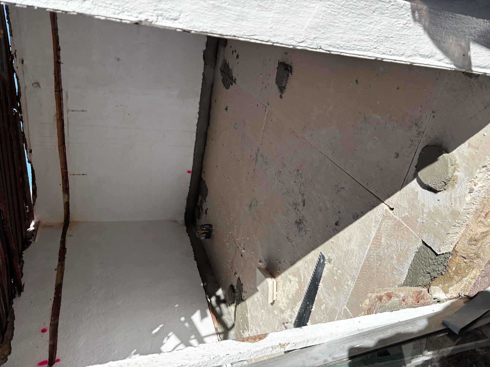 A small room with old wooden ceiling slats, new floor tiles being set in wet mortar, a laser level and a saw on the floor.