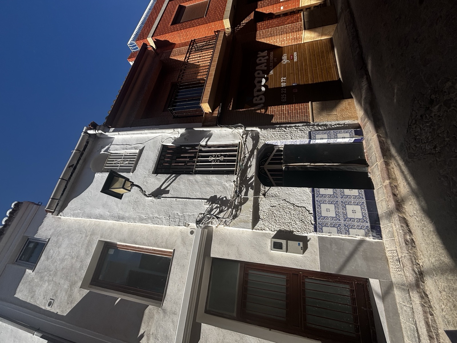 The house on the street: weathered white façade, dark green arched doors, iron window bars, and a hanging lantern.