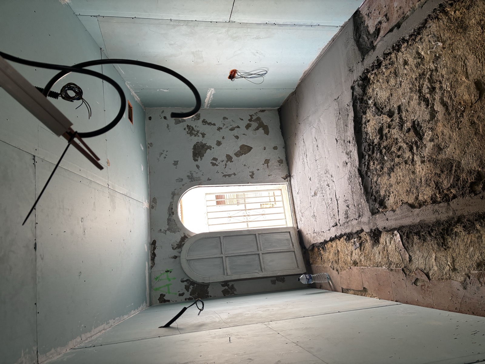 A narrow hallway mid-works: new drywall, a dug-out floor, an arched door leaning beside the opening to the street.